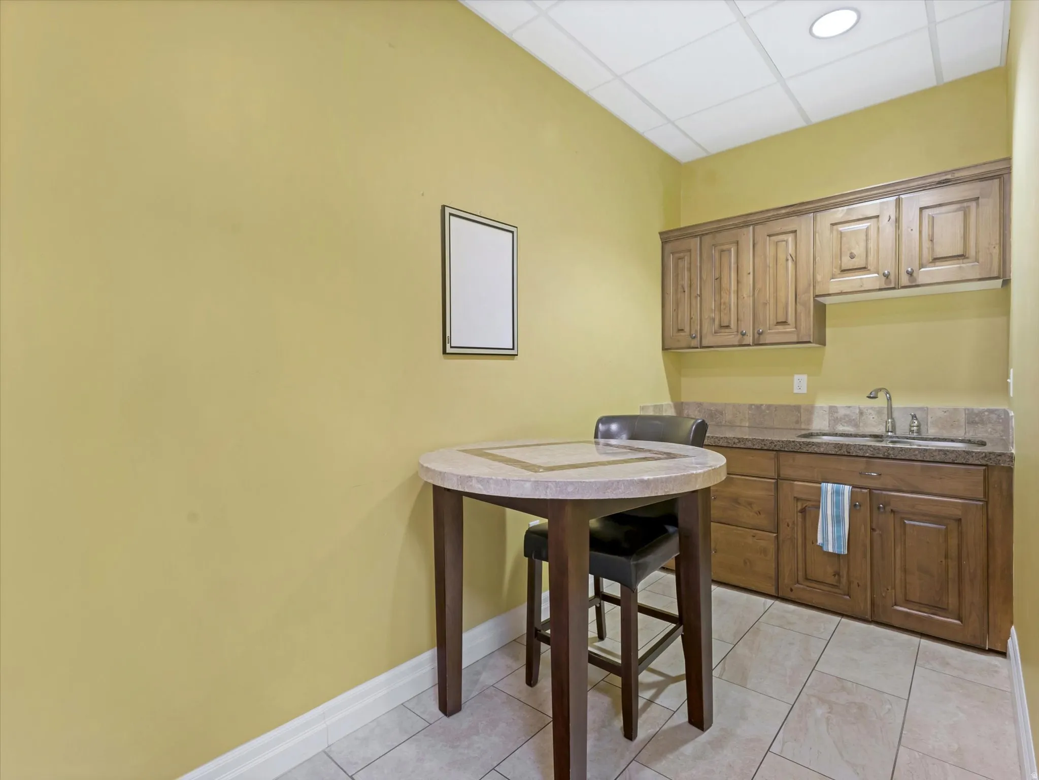 Kitchen with a paneled ceiling, wood finish cabinets, dark countertops, and light tile patterned flooring