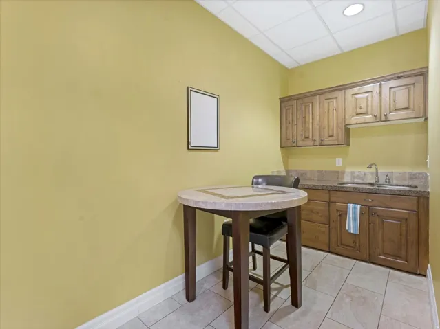 Kitchen with a paneled ceiling, wood finish cabinets, dark countertops, and light tile patterned flooring