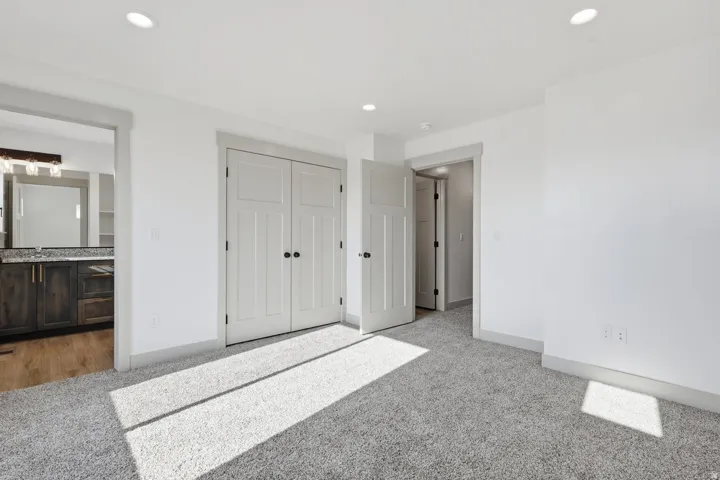 Unfurnished bedroom featuring light carpet, ensuite bath, a closet, and recessed lighting