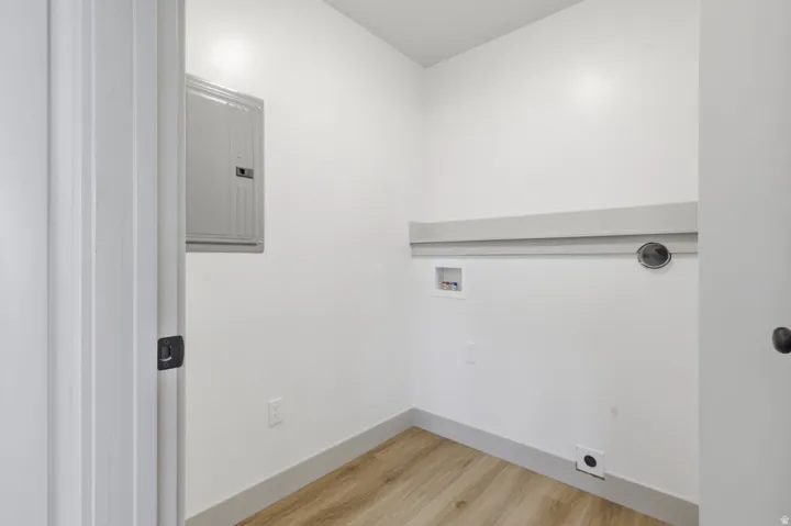 Laundry room with electric panel, light wood-style floors, and hookup for a washing machine