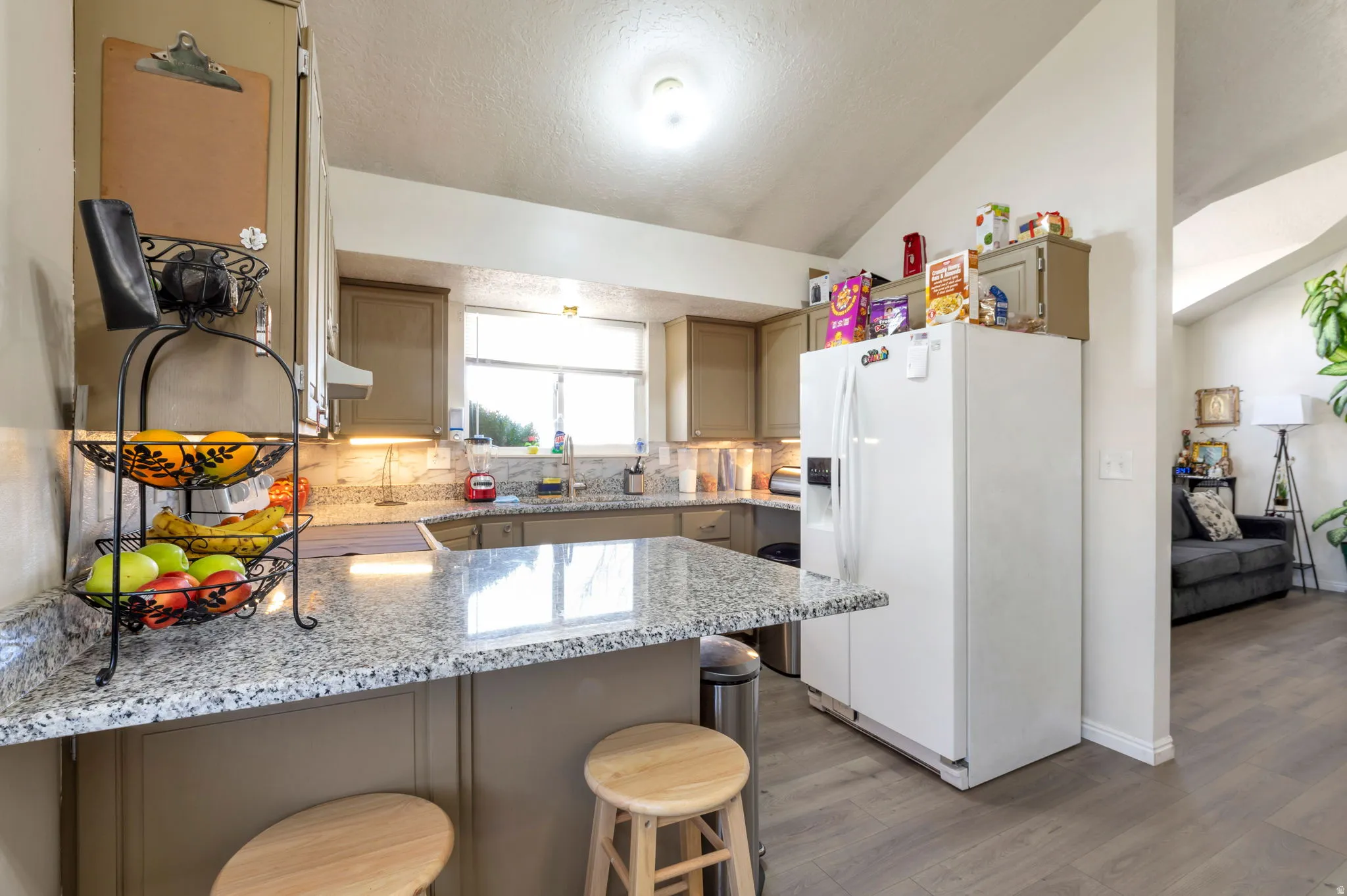 Kitchen with white fridge with ice dispenser, a peninsula, decorative backsplash, light wood-style flooring, and a kitchen bar