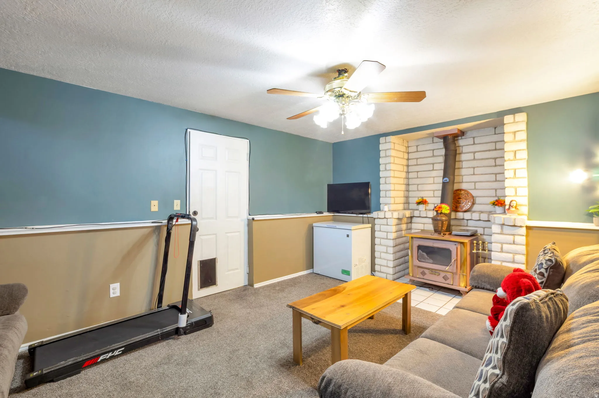 Carpeted living area featuring a ceiling fan, a textured ceiling, and a wood stove