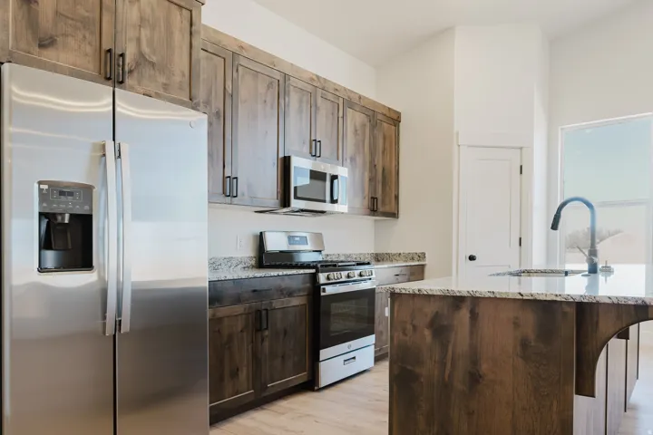 Kitchen with stainless steel appliances, light stone countertops, light wood-type flooring, and dark wood finish cabinetry
