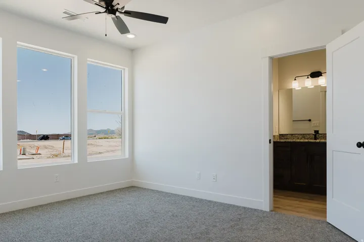 Unfurnished bedroom with light colored carpet, ceiling fan, and connected bathroom