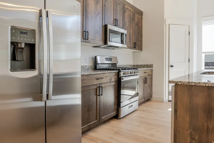 Kitchen featuring stainless steel appliances, light stone countertops, light wood-type flooring, and dark wood finish cabinetry