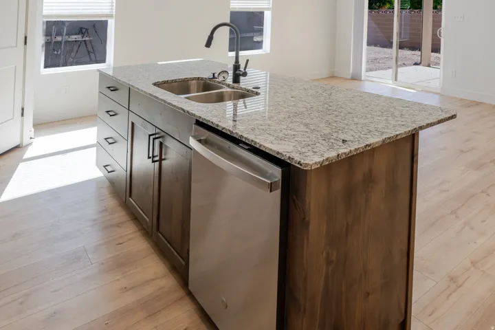 Kitchen featuring light wood-type flooring, light stone countertops, dishwasher, and an island with sink