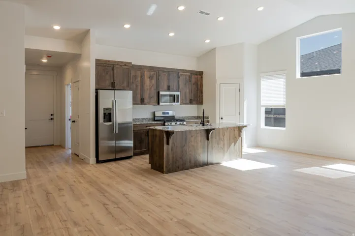 Kitchen with dark stone countertops, a breakfast bar area, stainless steel appliances, dark wood finish cabinets, and a kitchen island with sink