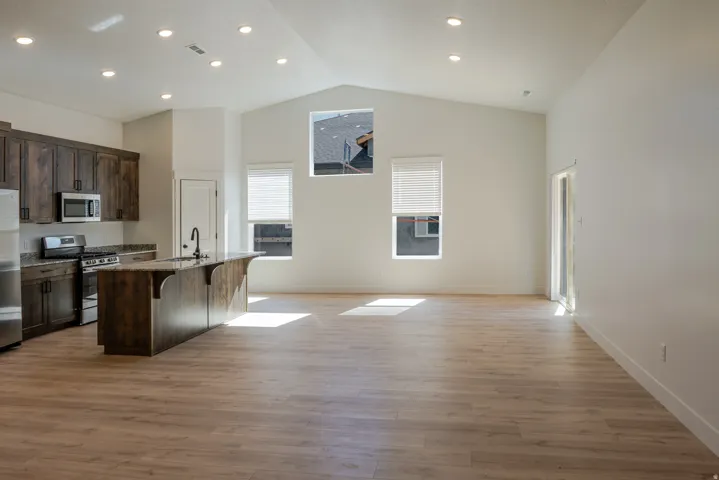 Kitchen with stainless steel appliances, a kitchen bar, open floor plan, a center island with sink, and light stone countertops