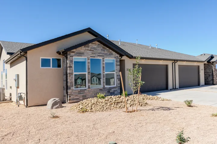 View of front of property with stone siding, driveway, stucco siding, an attached garage, and roof with shingles