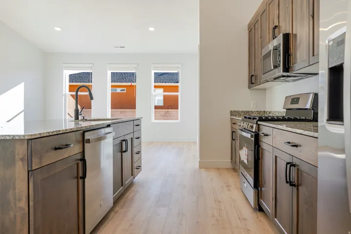 Kitchen featuring stainless steel appliances, light stone countertops, light wood-style flooring, recessed lighting, and a center island with sink