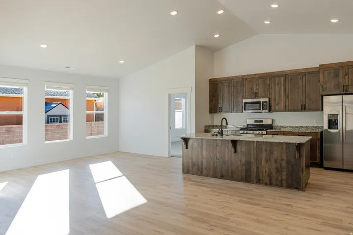 Kitchen featuring light stone countertops, stainless steel appliances, a kitchen bar, dark wood finish cabinets, and a center island with sink