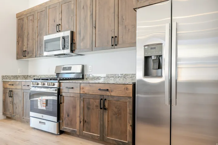 Kitchen featuring stainless steel appliances, light stone counters, wood finish cabinetry, and light wood finished floors