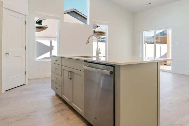 Kitchen featuring a center island with sink, dishwasher, light wood finished floors, light stone countertops, and gray cabinets