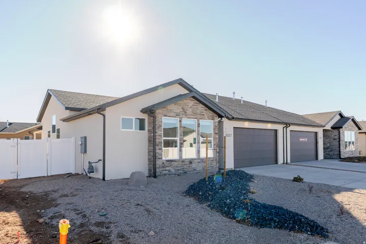 Ranch-style house with stucco siding, stone siding, driveway, and a gate