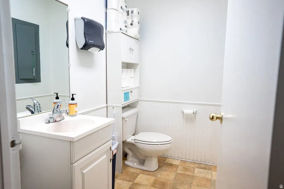 Bathroom with vanity, electric panel, wainscoting, and stone finish flooring