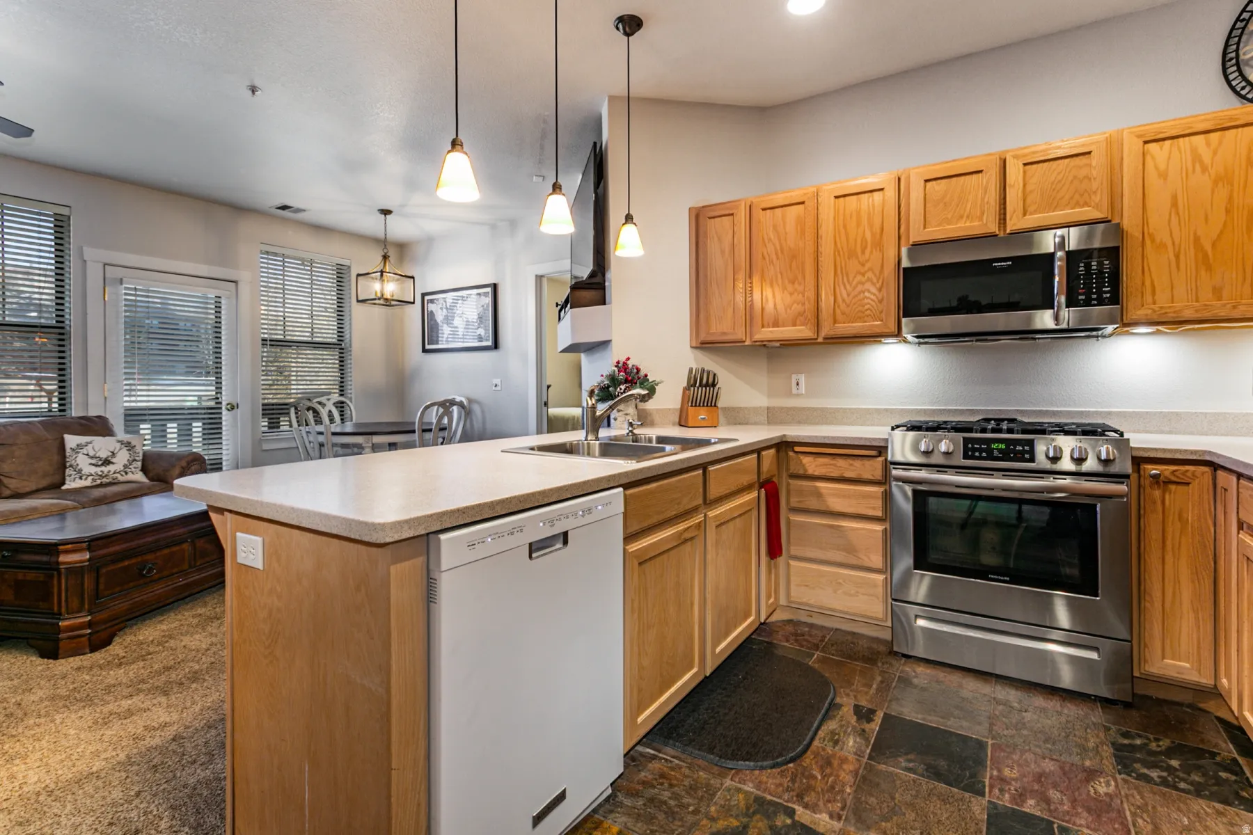 Kitchen with stainless steel appliances, open floor plan, a peninsula, decorative light fixtures, and dark stone finish flooring