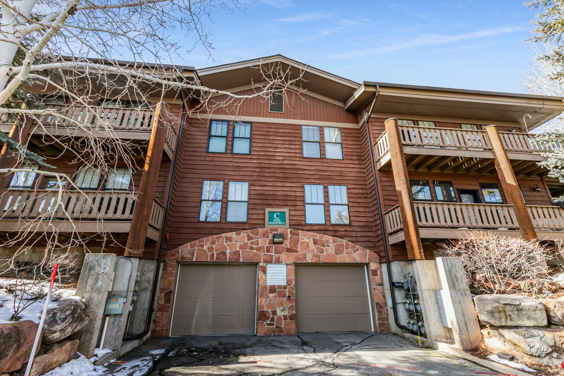 Rear view of property featuring an attached garage, a balcony, driveway, and stone siding
