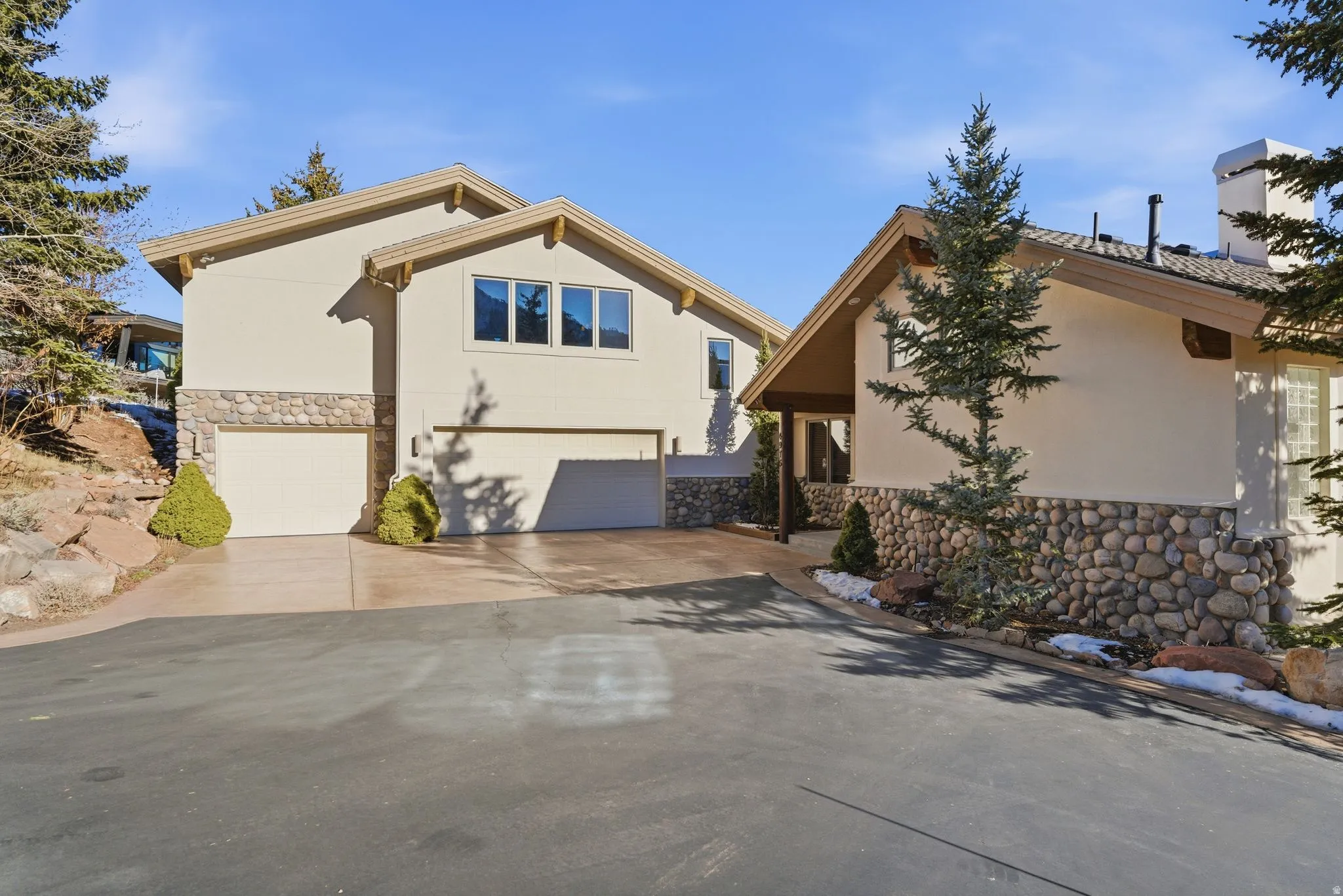 View of front facade with stone siding, an attached garage, stucco siding, and driveway
