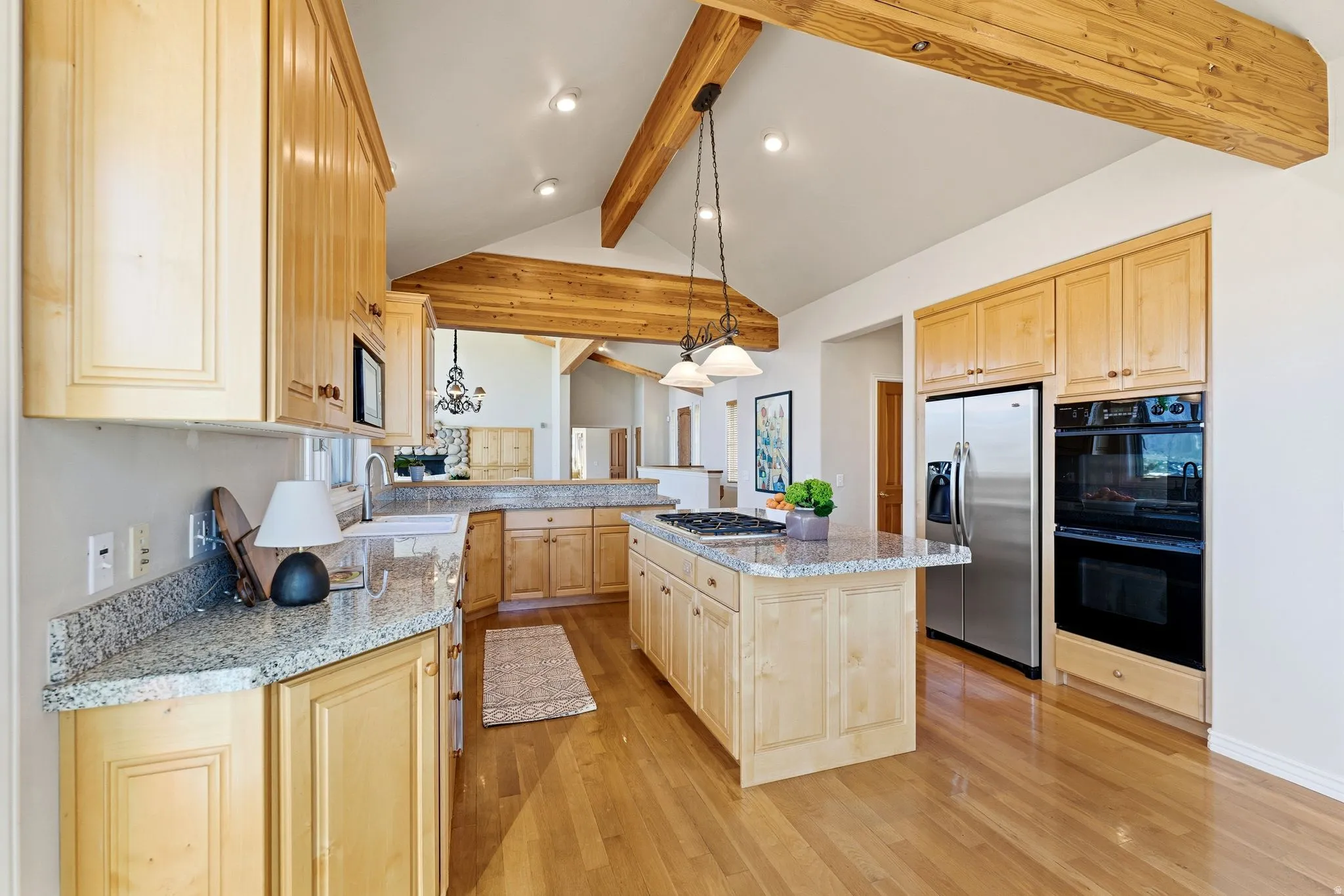 Kitchen with light wood finish cabinets, hanging light fixtures, stainless steel appliances, beam ceiling, and a kitchen island