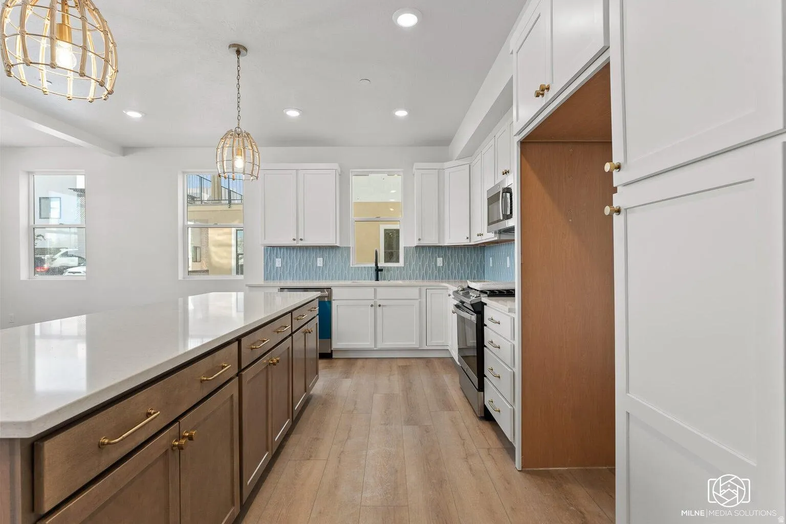 Kitchen featuring two tone cabinets, decorative light fixtures, light wood finished floors, decorative backsplash, and stainless steel appliances