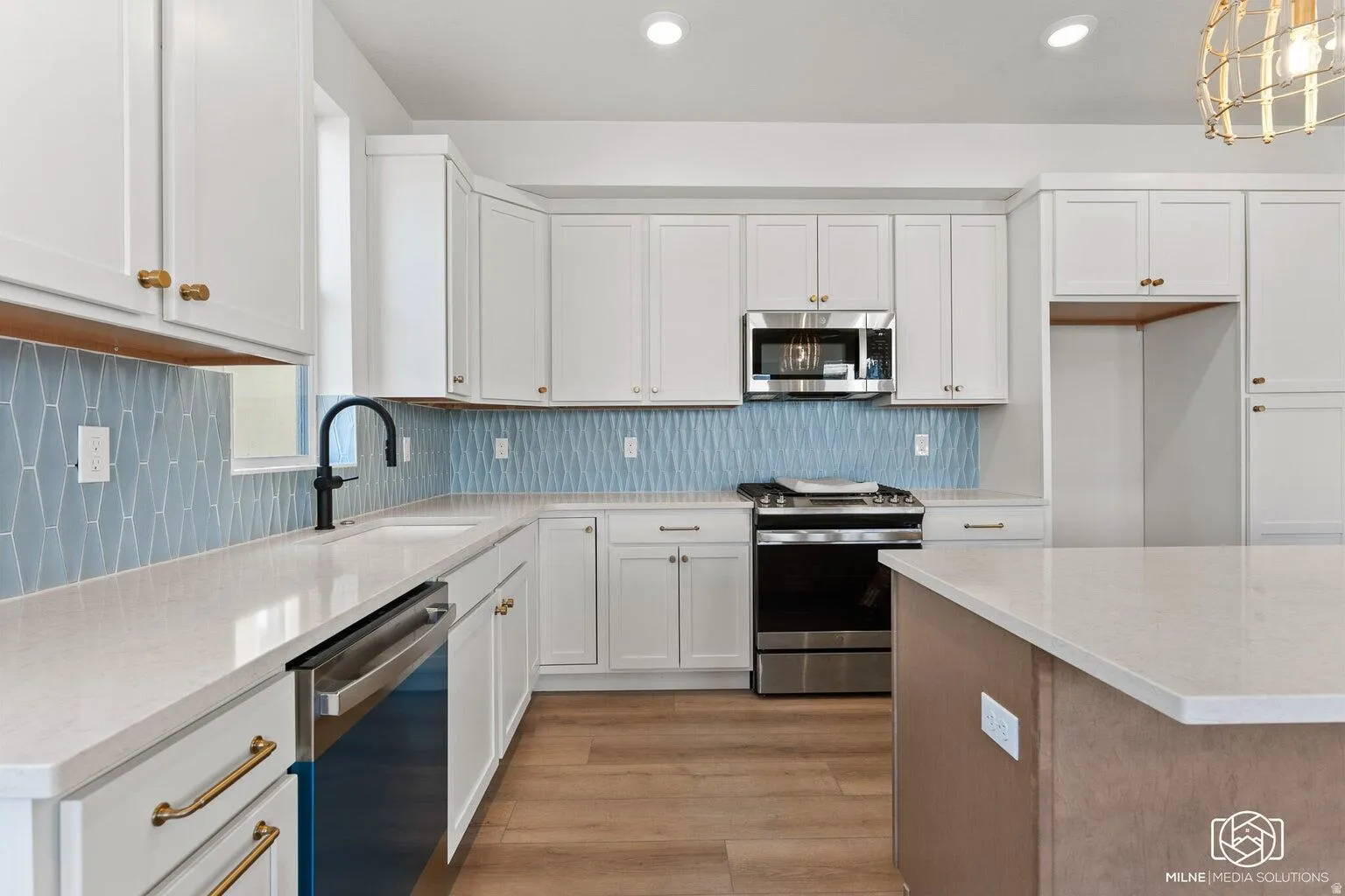 Kitchen featuring stainless steel appliances, light stone counters, light wood-type flooring, decorative backsplash, and two tone cabinets