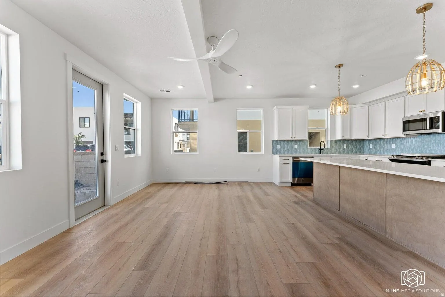 Kitchen with hanging light fixtures, tasteful backsplash, two tone color scheme, light wood finished floors, and stainless steel appliances