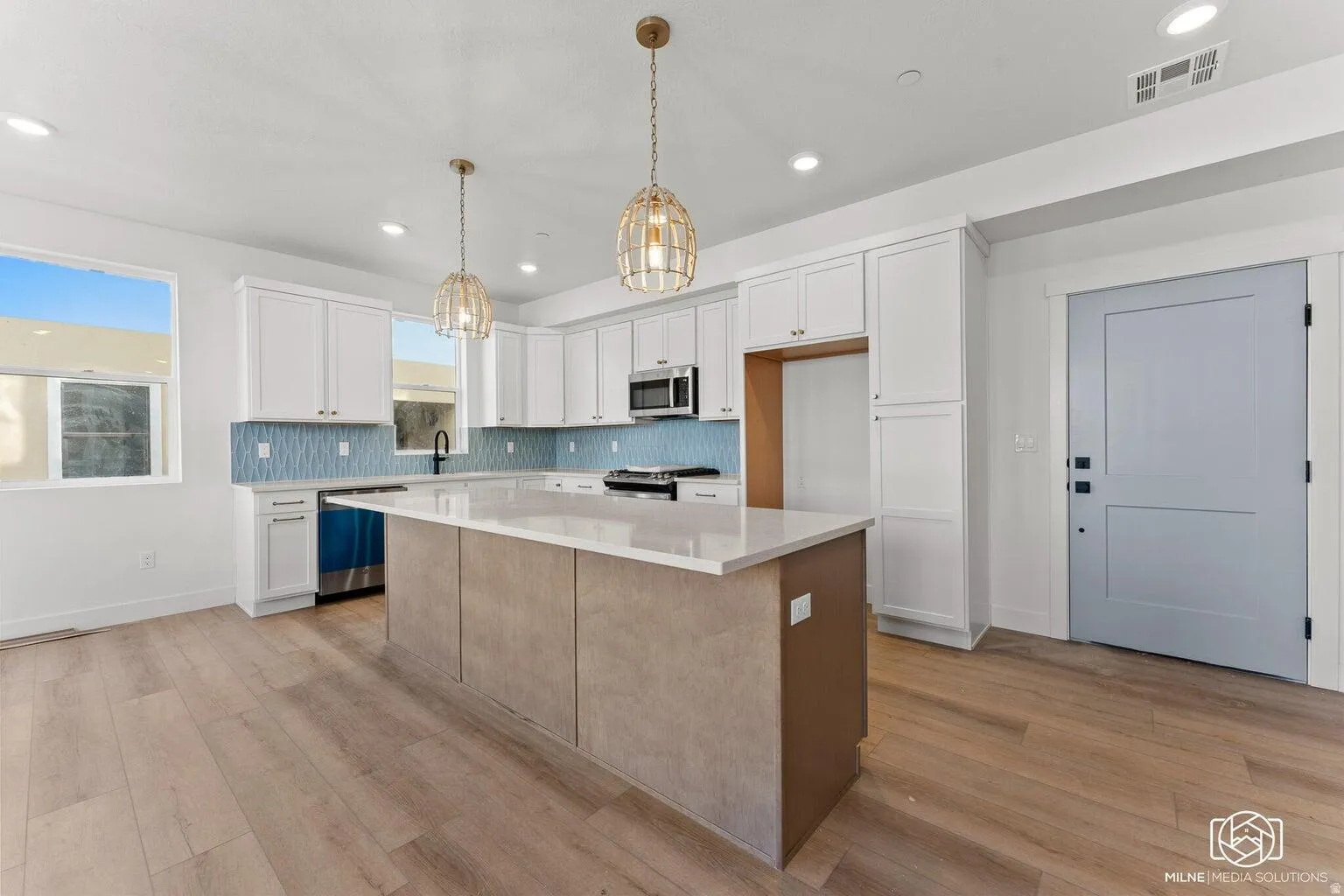 Two tone kitchen featuring a center island, two tone color scheme, pendant lighting, light wood-style flooring, and light stone countertops