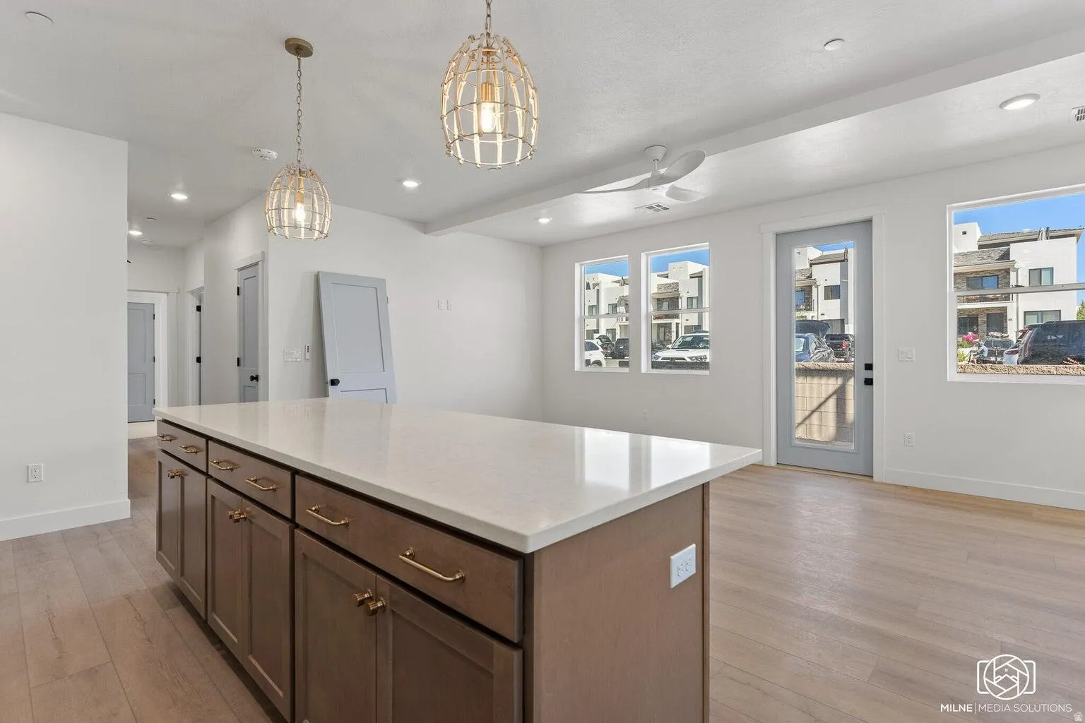 Kitchen with light wood-style flooring, a kitchen island, pendant lighting, dark wood finish cabinets, and light stone countertops