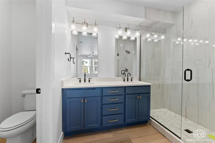 Bathroom with a shower stall, double vanity, light wood-type flooring, and a ceiling fan