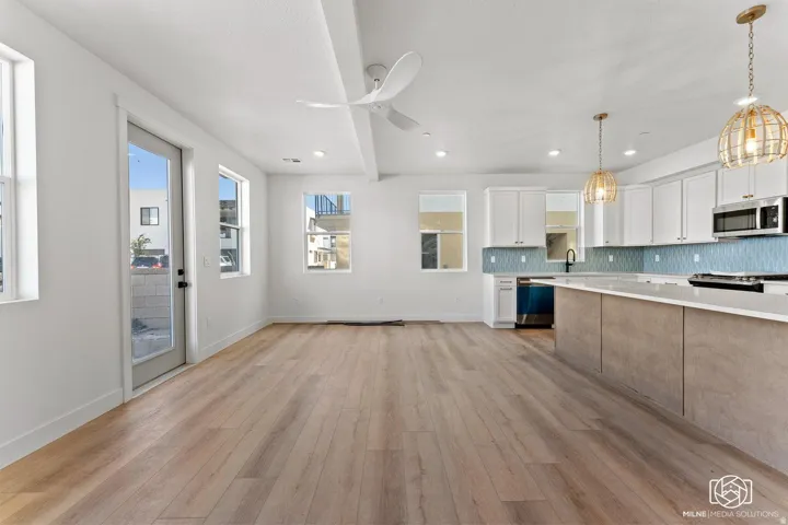 Kitchen with hanging light fixtures, tasteful backsplash, two tone color scheme, light wood finished floors, and stainless steel appliances