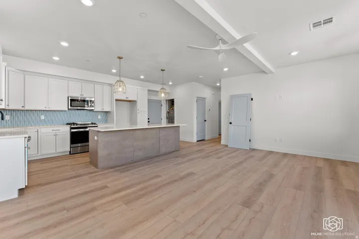 Dual tone kitchen featuring stainless steel appliances, pendant lighting, a kitchen island, beamed ceiling, and open floor plan