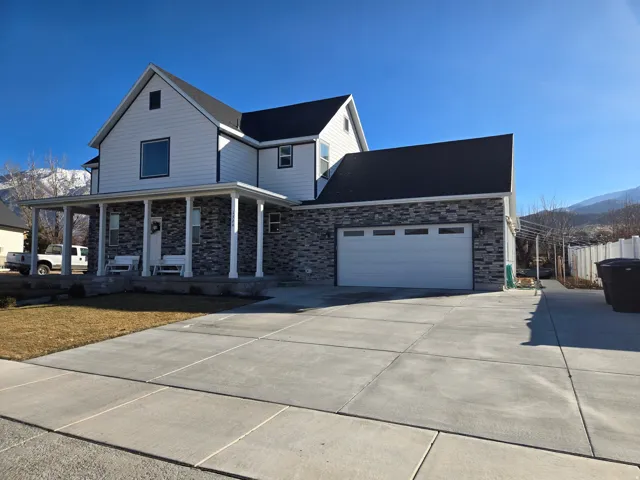 View of front of property featuring covered porch, stone siding, concrete driveway, a garage, and a mountain view