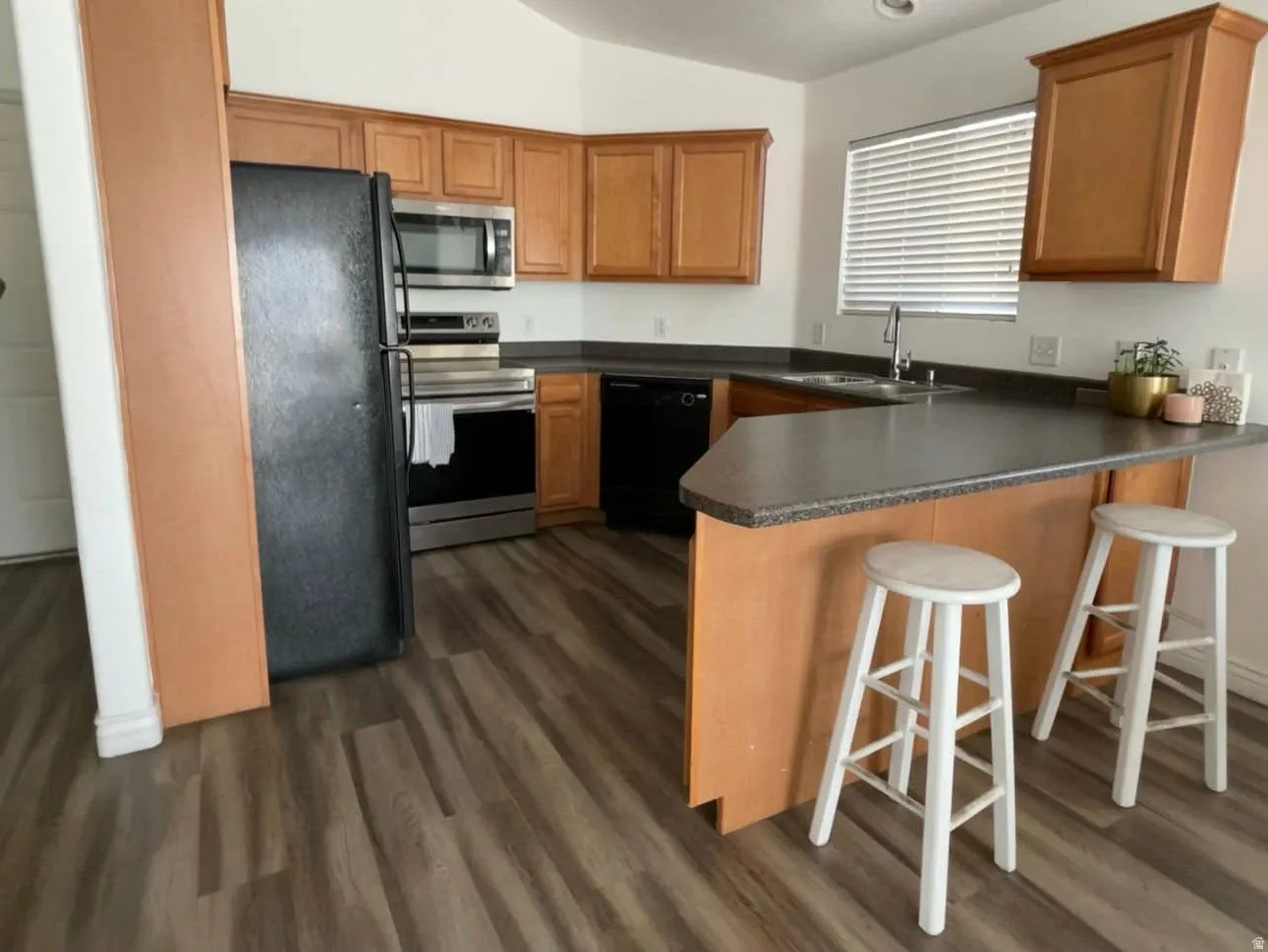 Kitchen with a peninsula, black appliances, dark countertops, lofted ceiling, and a breakfast bar