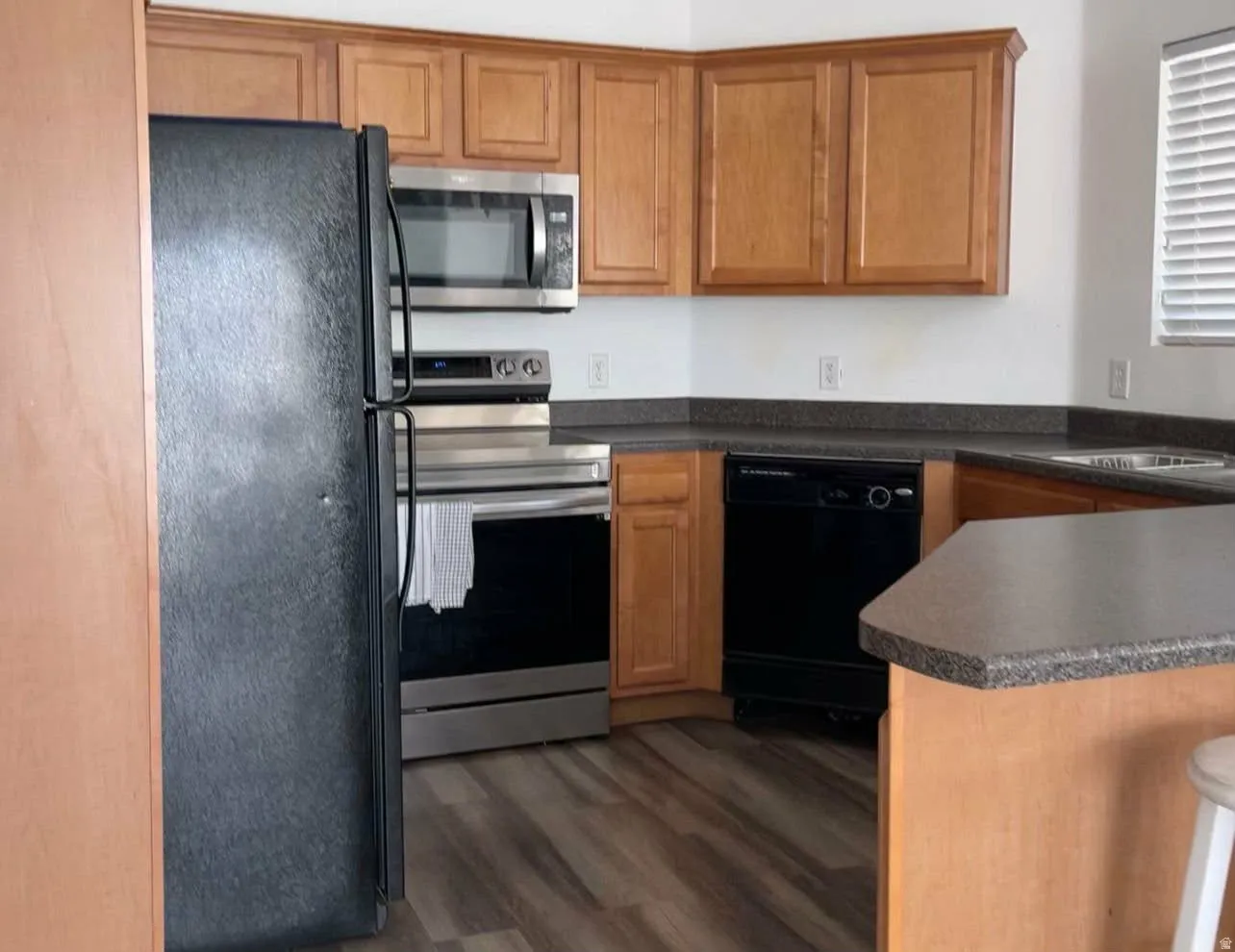 Kitchen featuring black appliances, dark countertops, a peninsula, dark wood-style floors, and wood finish cabinetry