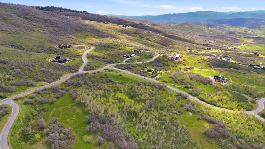 Expansive natural landscape featuring rolling hills, scattered trees, paved roads, and several residential structures nestled within the terrain