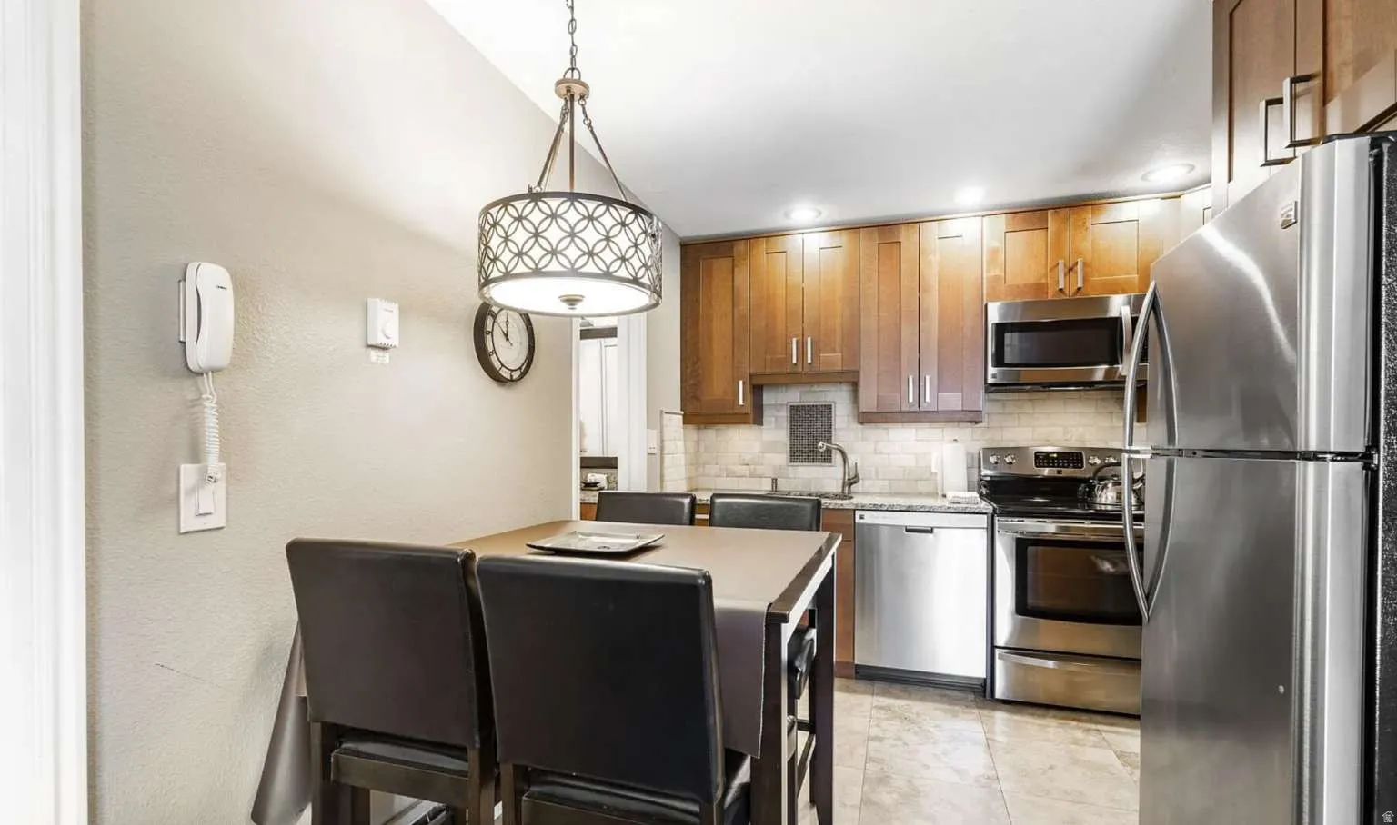 Kitchen with stainless steel appliances, hanging light fixtures, wood finish cabinets, a textured wall, and backsplash