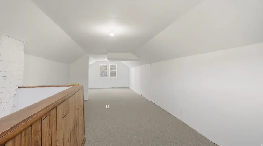 Hallway with lofted ceiling and light colored carpet