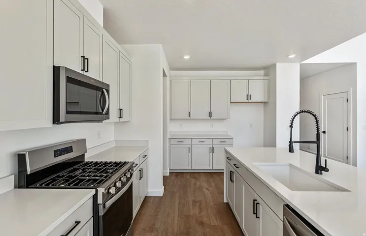 Kitchen with stainless steel appliances, dark wood-type flooring, white cabinets, recessed lighting, and light stone counters