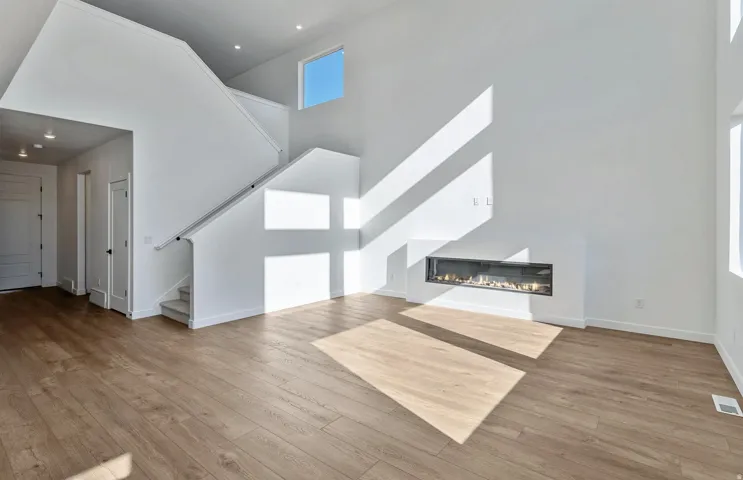 Unfurnished living room featuring a high ceiling, light wood-style floors, and a glass covered fireplace