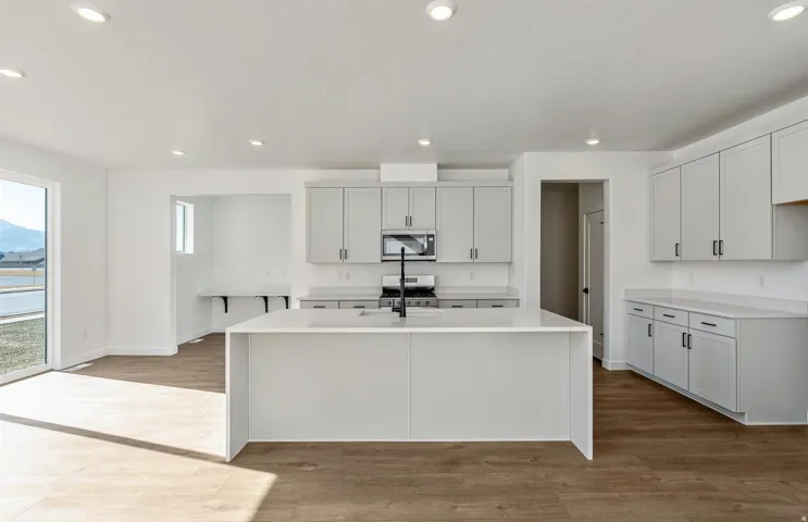 Kitchen with light wood-style flooring, light stone counters, stainless steel appliances, an island with sink, and white cabinets