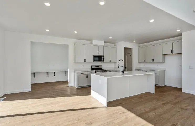 Kitchen featuring light wood-style flooring, a center island with sink, stainless steel appliances, recessed lighting, and light stone counters
