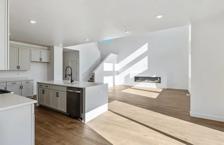 Kitchen featuring dark wood-style flooring, a center island with sink, a glass covered fireplace, light stone countertops, and recessed lighting