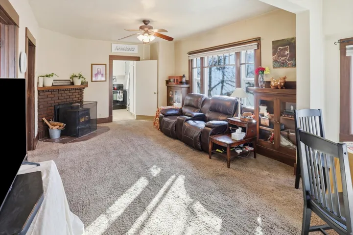 Living room featuring light carpet, ceiling fan, and a wood stove