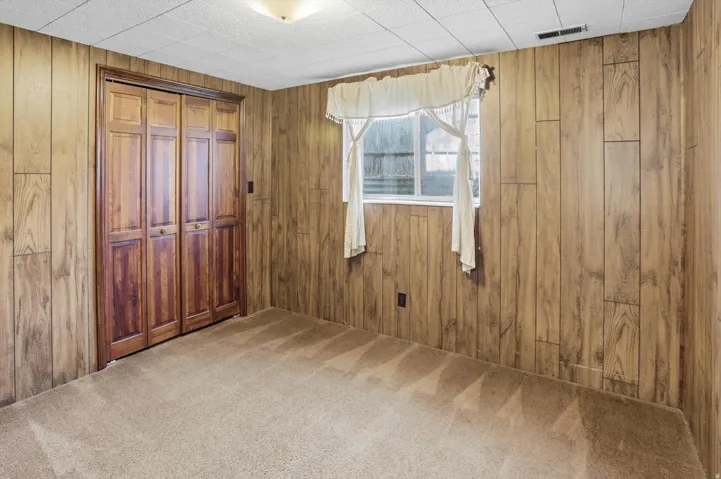 Bedroom with carpet flooring, a closet, and wood walls