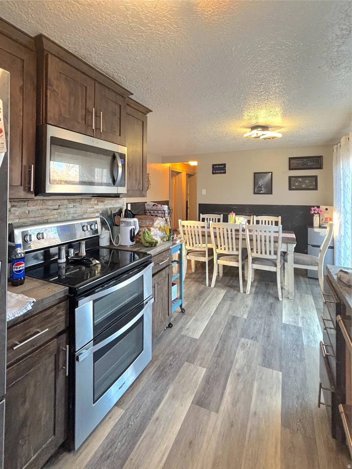 Kitchen featuring stainless steel appliances, dark wood finish cabinets, dark wood-type flooring, a textured ceiling, and backsplash