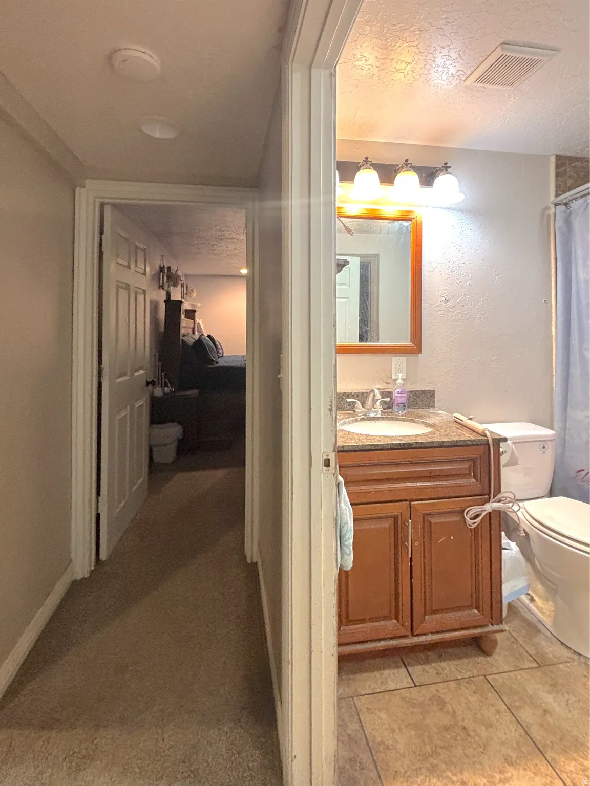 Full bath with a textured ceiling, vanity, curtained shower, and a textured wall