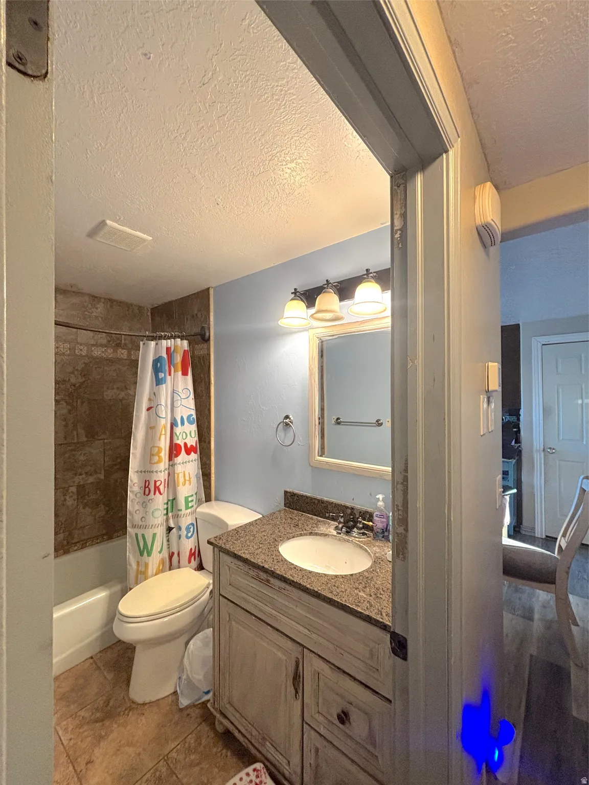 Full bath with a textured ceiling, vanity, and shower / bath combo with shower curtain