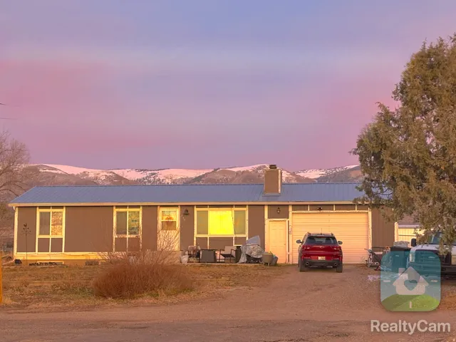 Ranch-style house with a metal roof, dirt driveway, a mountain view, an attached garage, and a chimney
