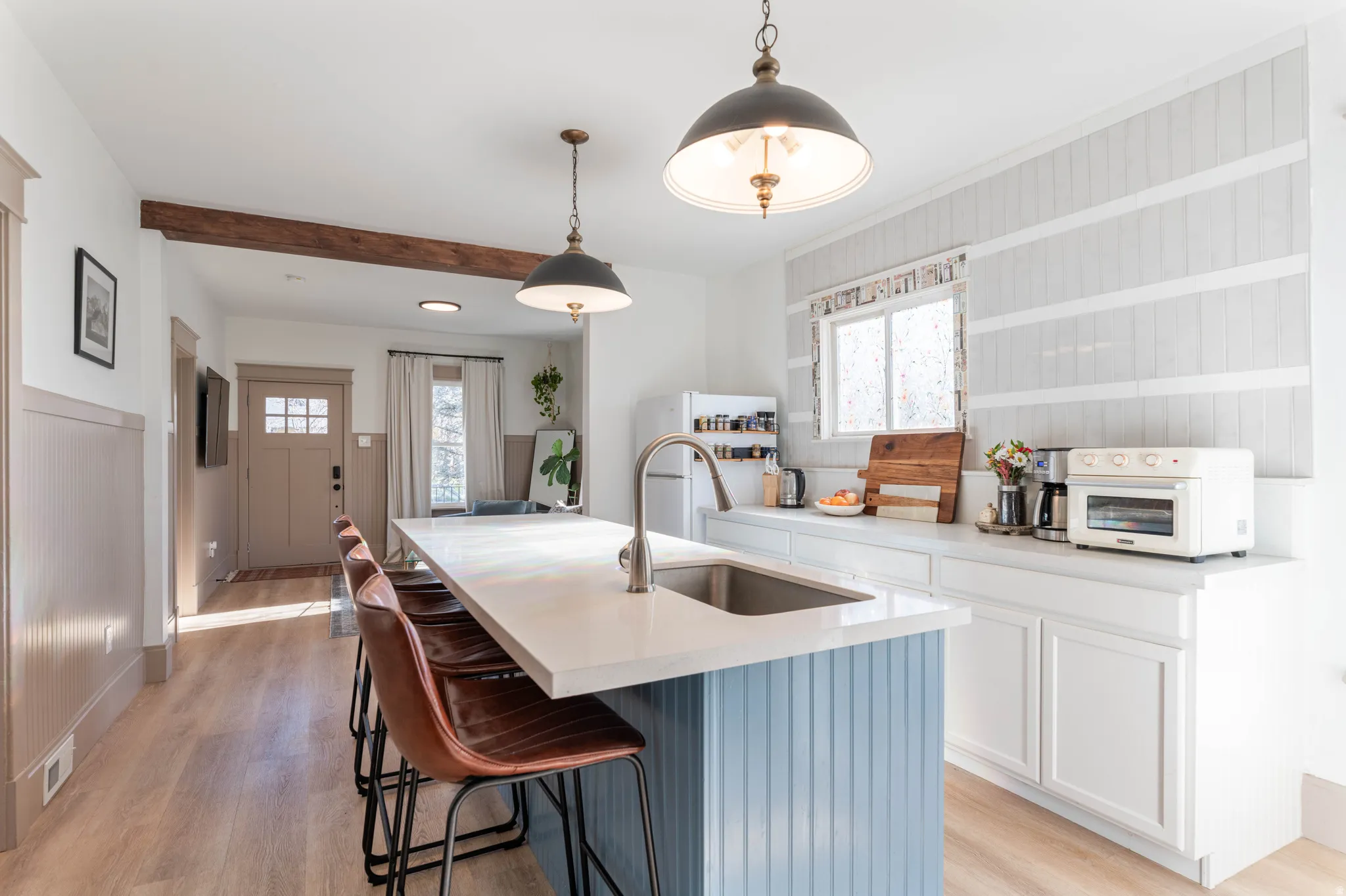Dual tone kitchen featuring a breakfast bar area, decorative light fixtures, light wood finished floors, a kitchen island with sink, and healthy amount of natural light