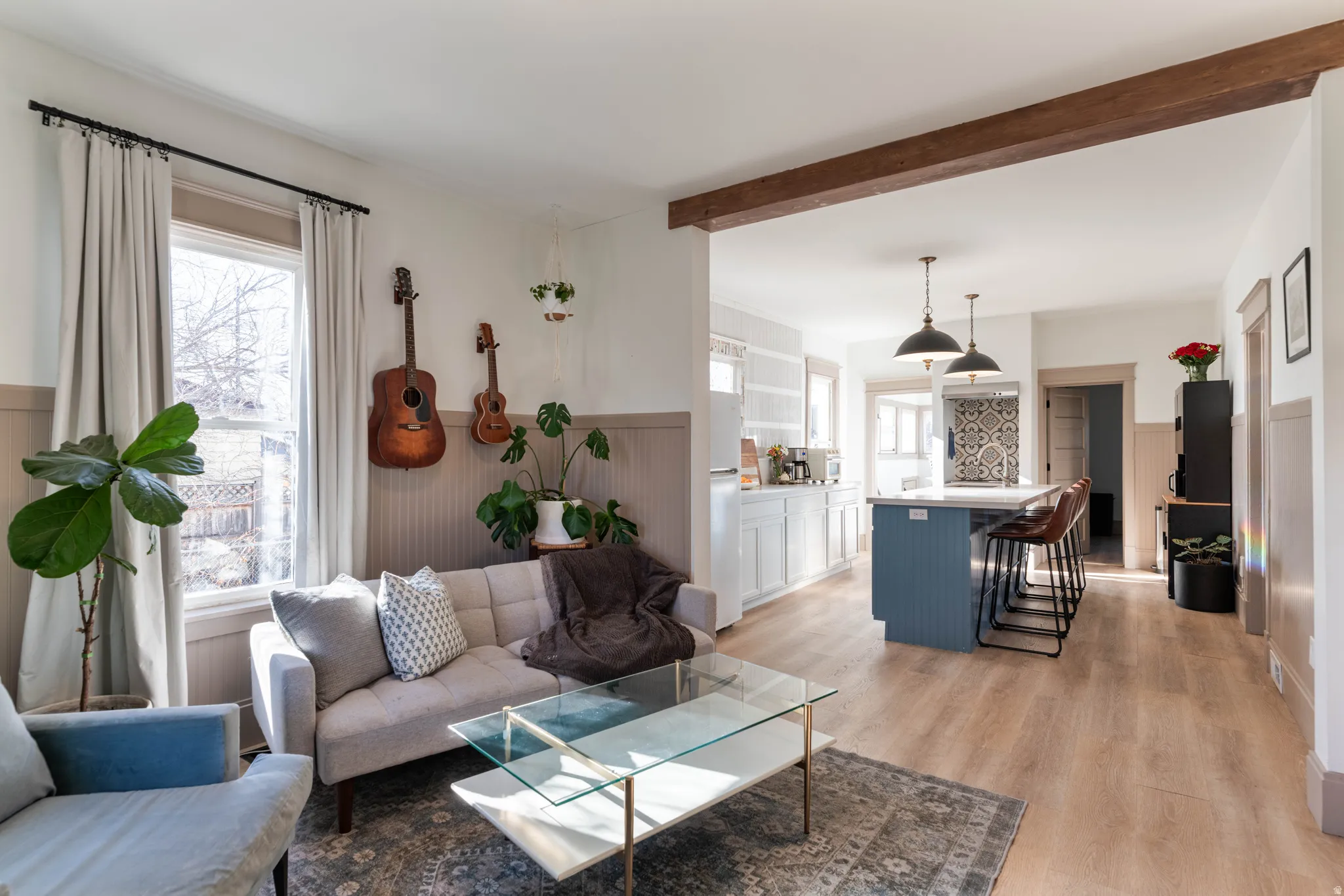 Living area featuring wainscoting, light wood-style floors, healthy amount of natural light, beamed ceiling, and a decorative wall